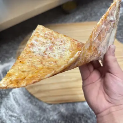 A hand holding a cheese slice that stays straight with no flop
